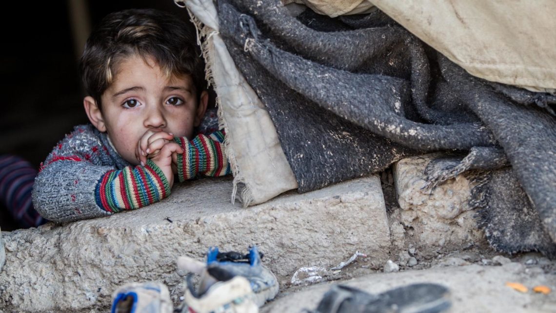 Iraq, February 2014.  3 year old Hakim is peeping out a worn tent in the Domiz refugee camp in Northern Iraq.
(children's names have been changed)

Notes from the field:

We saw a small boy (Hakim, 3  name changed) peeping out of a worn tent. Inside, we met his mother (Fatema) and younger sister, along with a pregnant family friend. The two women are friends and neighbours in the camp. They have been in Domiz for a year.

o	Life in the camp: They were worried about the condition of their tents. The most afraid of the storms in Domiz because their tent wont withstand it. They said they were worried, lonely, cold, tired and a bit fed up because there were things like no nappies. Being pregnant in the camp is difficult and the pregnant mother isnt having regular check-ups. They said the water provision was really good and that they had enough (UNICEF) blankets. They have been getting clean water and that was good.

o	Leaving Syria: The families left Syria because their husbands were being threatened with conscription and joining the military. Their husbands left Syria urgently. The pregnant mothers husband had to go without her or the children, leaving her to follow, with her little boy and only the items she could get on the donkey. Hakims family walked for three hours in the Winter to escape (at the time Hakim was 2 years old and his sister was just 5 months).

o	Life in Syria was terrifying. They talked about the explosions and about seeing men who had been slaughtered. Some of their friends had family members, where they had been slaughtered and then the family had been sent a video afterwards. There were also incidences of kidnapping of women as well. 

o	In Hakims home in Syria they had planted onions and enjoyed eating them  they cant do this any more. The children didn't understand anything that was happening in Syria, but they were still very frightened by the noises. They talked about how husbands would go out to get bread for